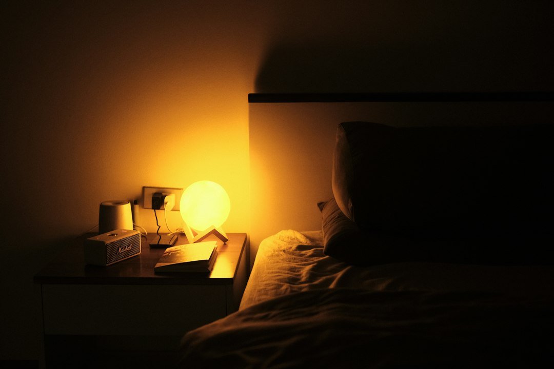 a night stand with a lamp on it next to a bed