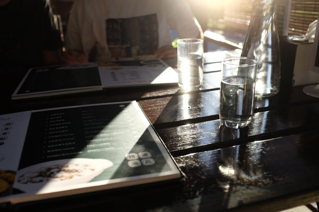 Two menus and glasses on a sunlit wooden table.